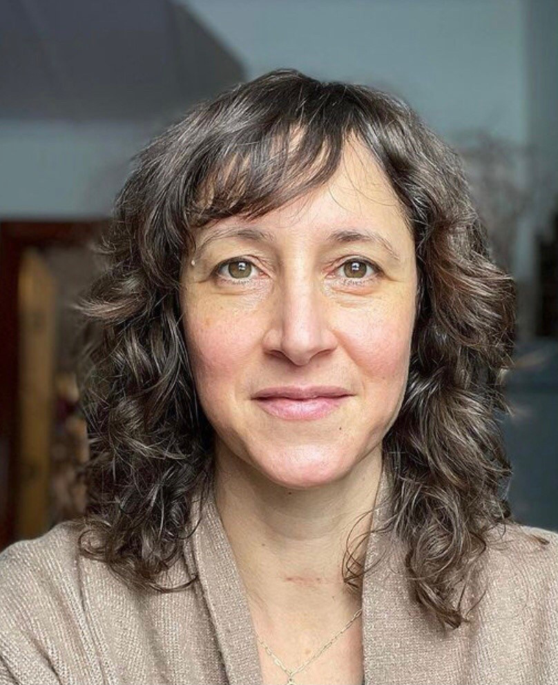 Susan Fauman looks at the camera while taking a selfie. The background behind her is blurred.