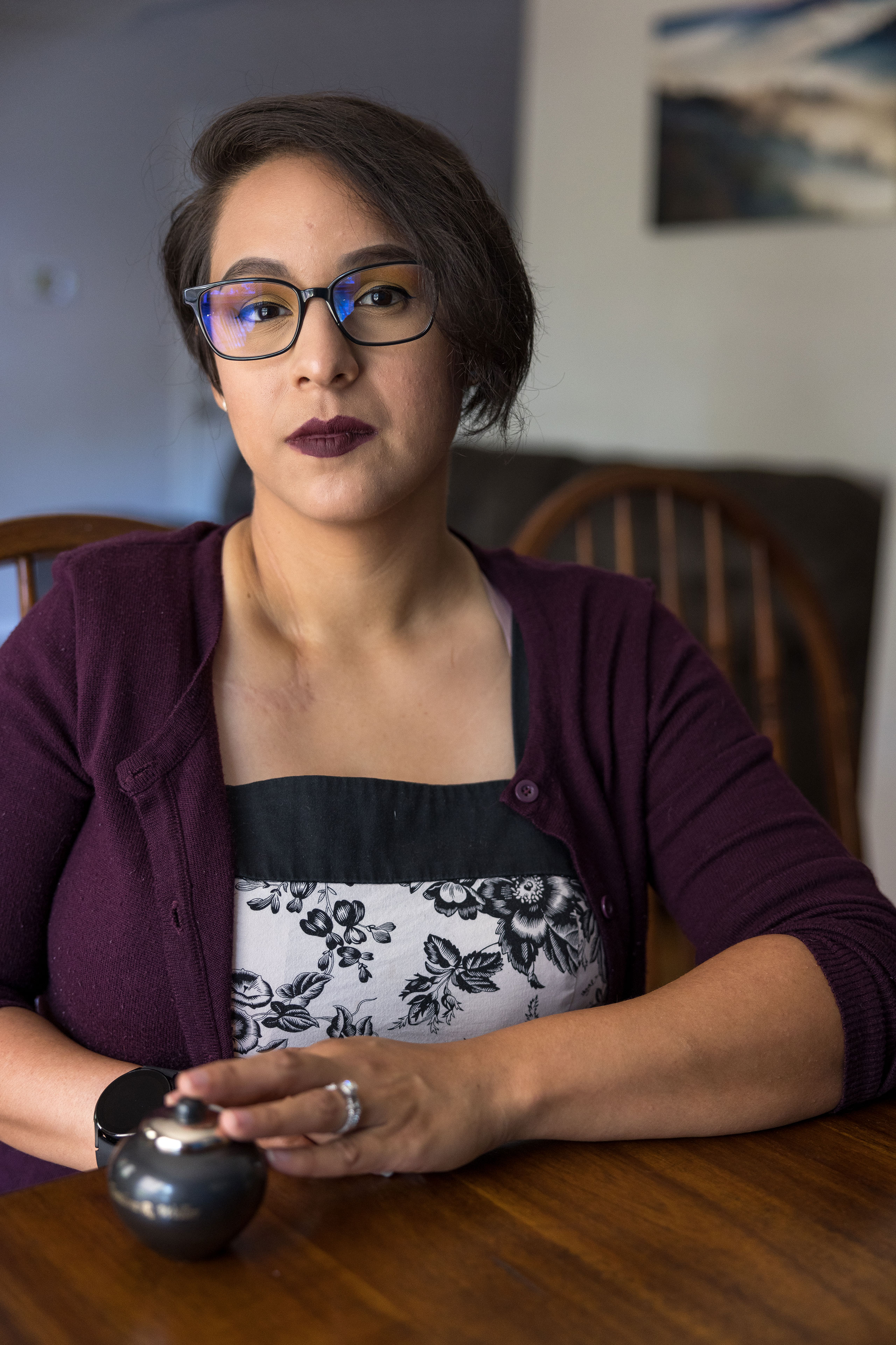 A woman sits at a table where a small urn is placed.