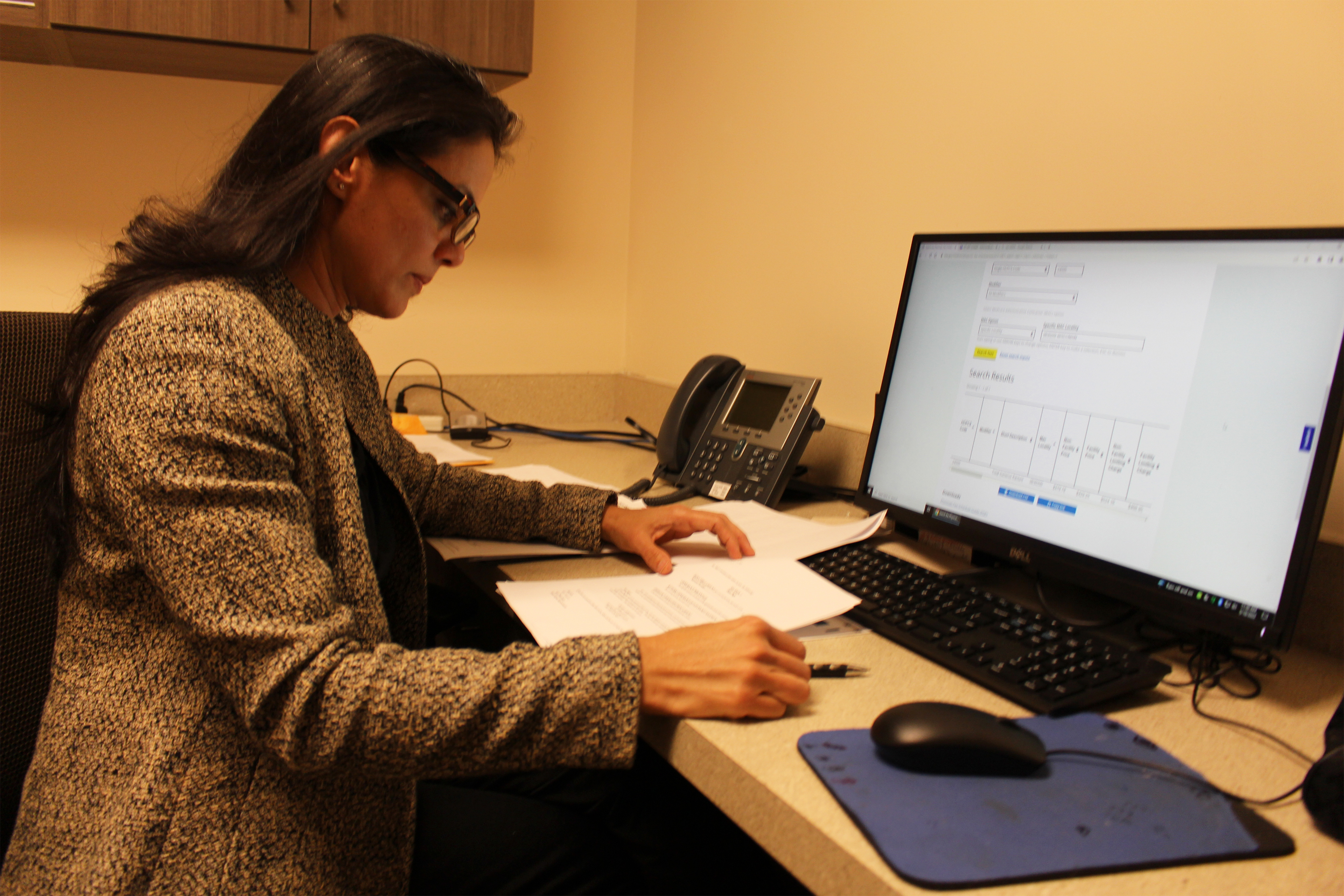 A photo shows Sunita Kalsariya sitting at a desk and working on a computer in an office.