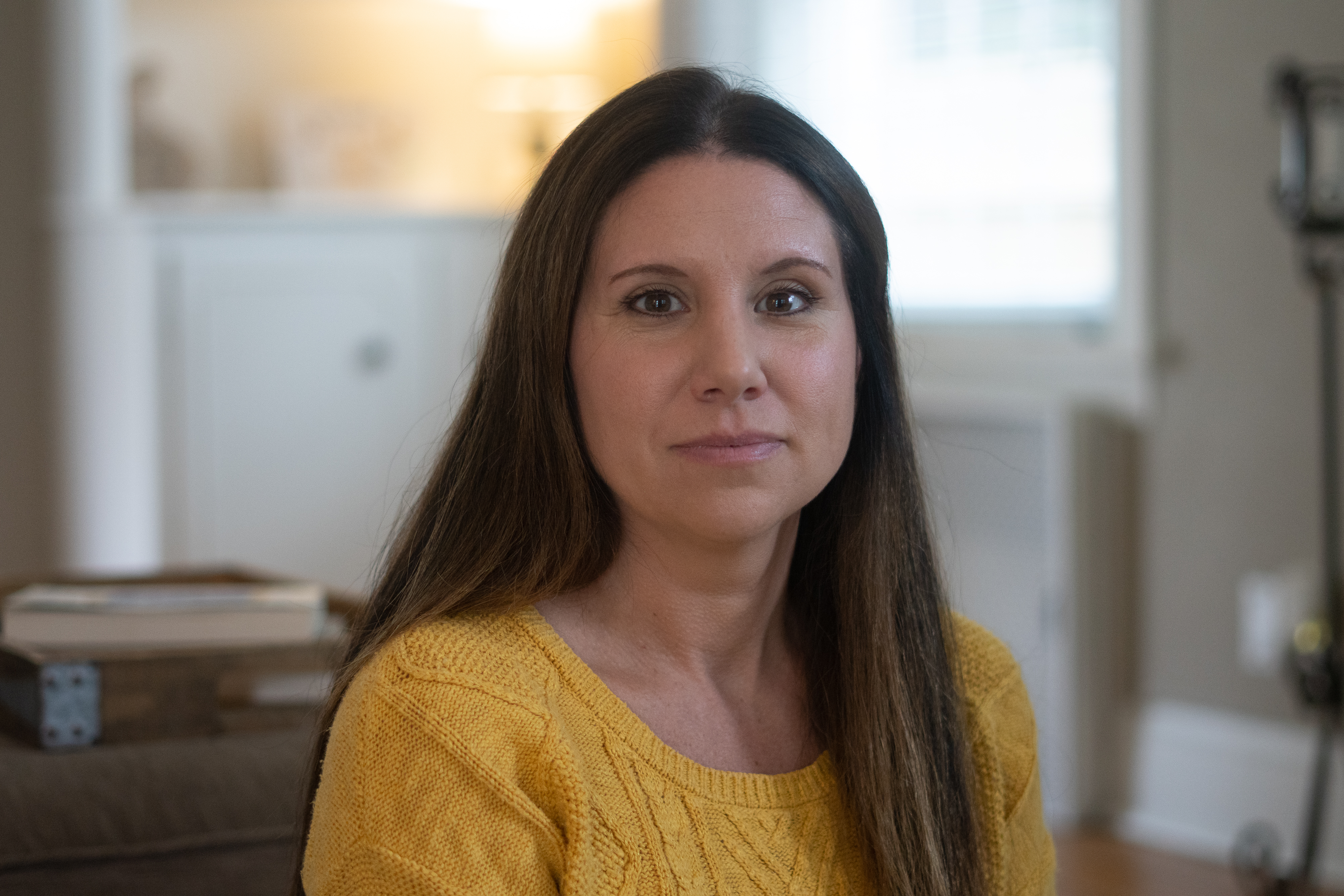 a woman with dark hair and eyes wears a yellow sweater and looks into the camera