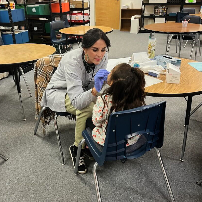 A photo of a dental worker examining a student sitting at a desk inside a mobile clinic.