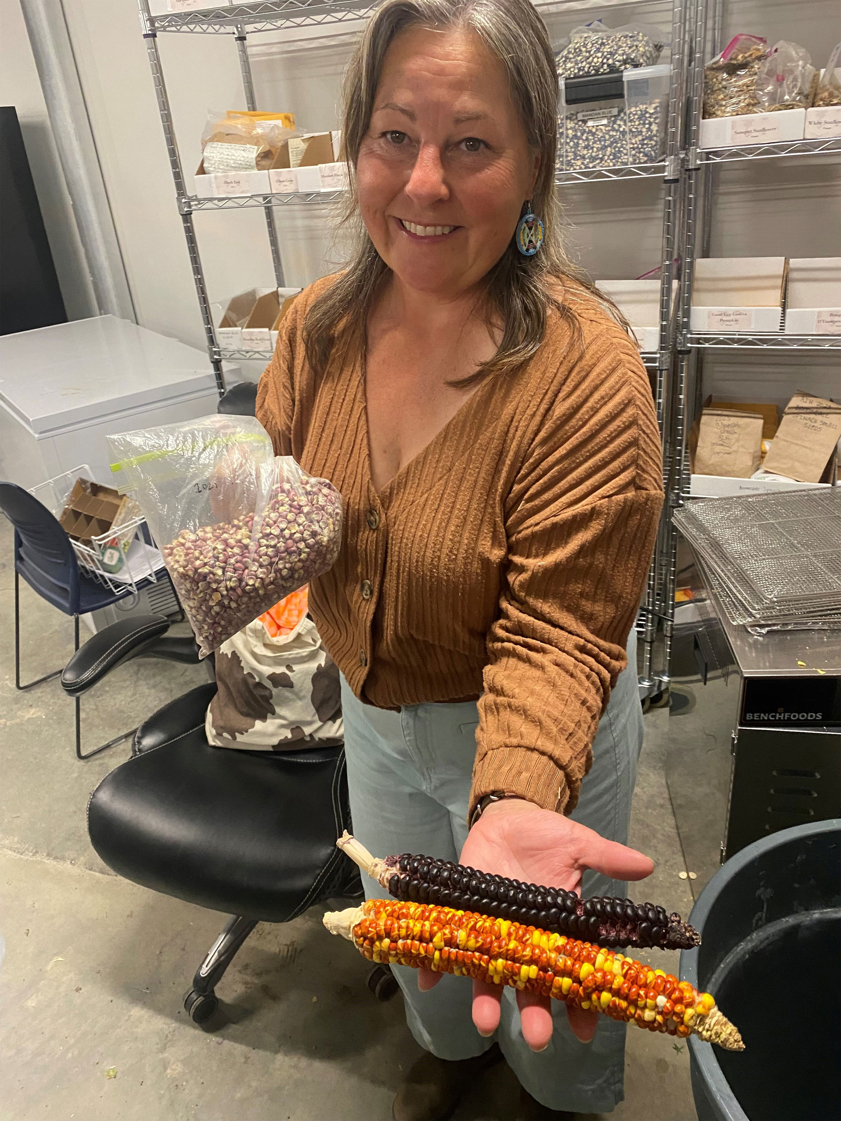 A photo of a woman holding ears of corn to the camera.
