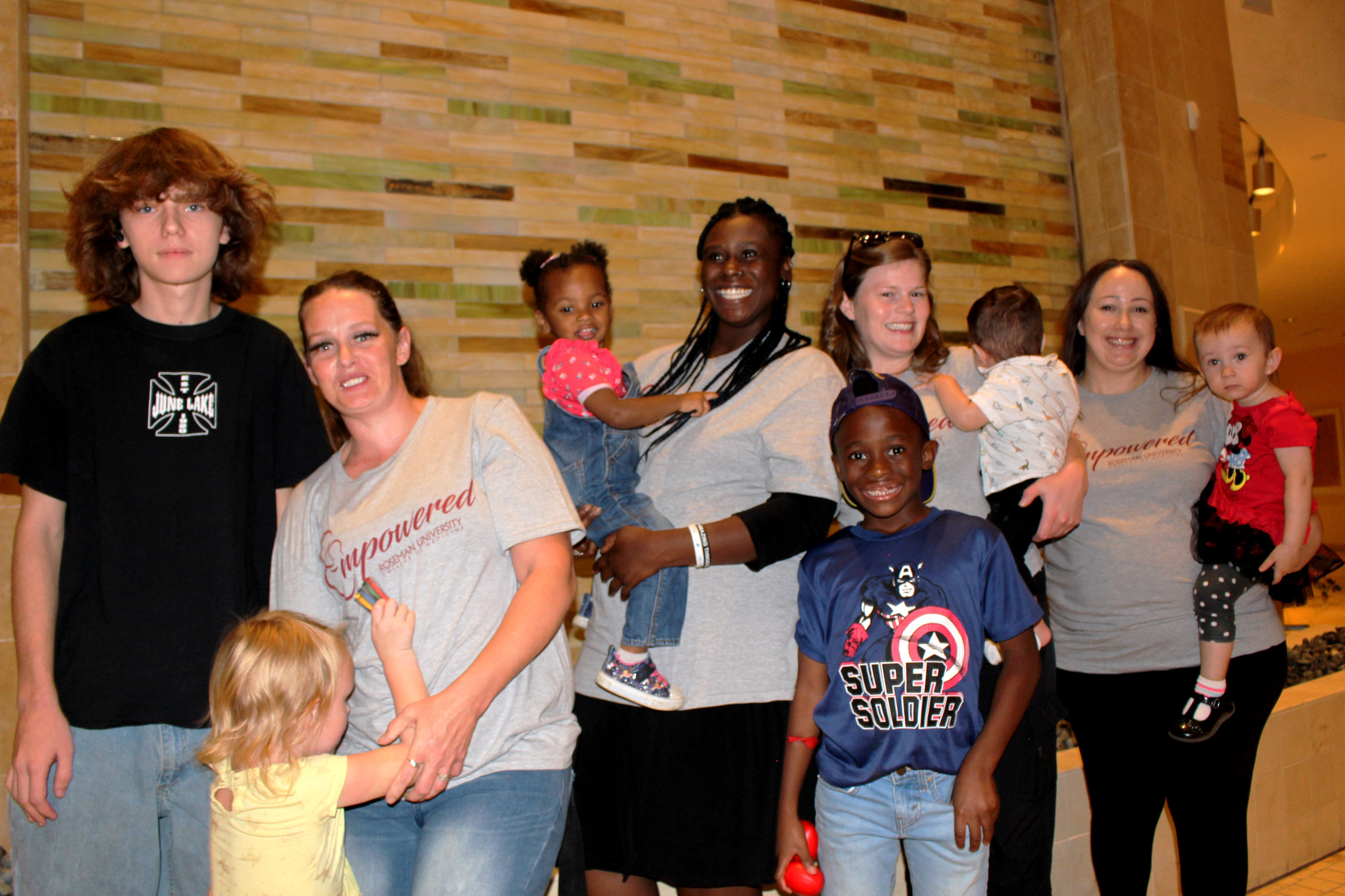 A photo of four mothers standing together and smiling for a photo alongside their children.
