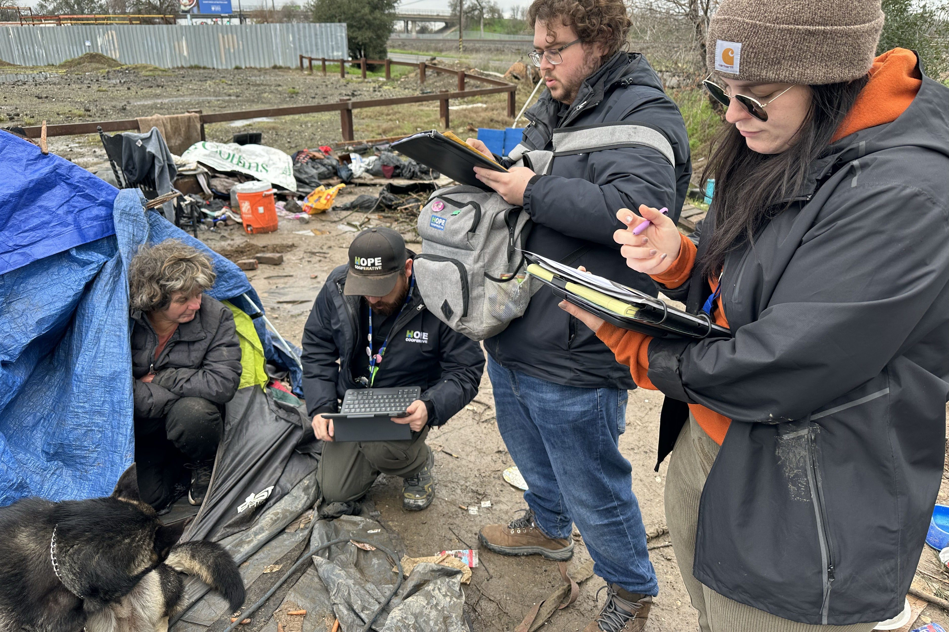 Outreach workers Greg Stupplebeen (from left), John Harding, and Afton Francik, speak with a person who is crouching in their tent.