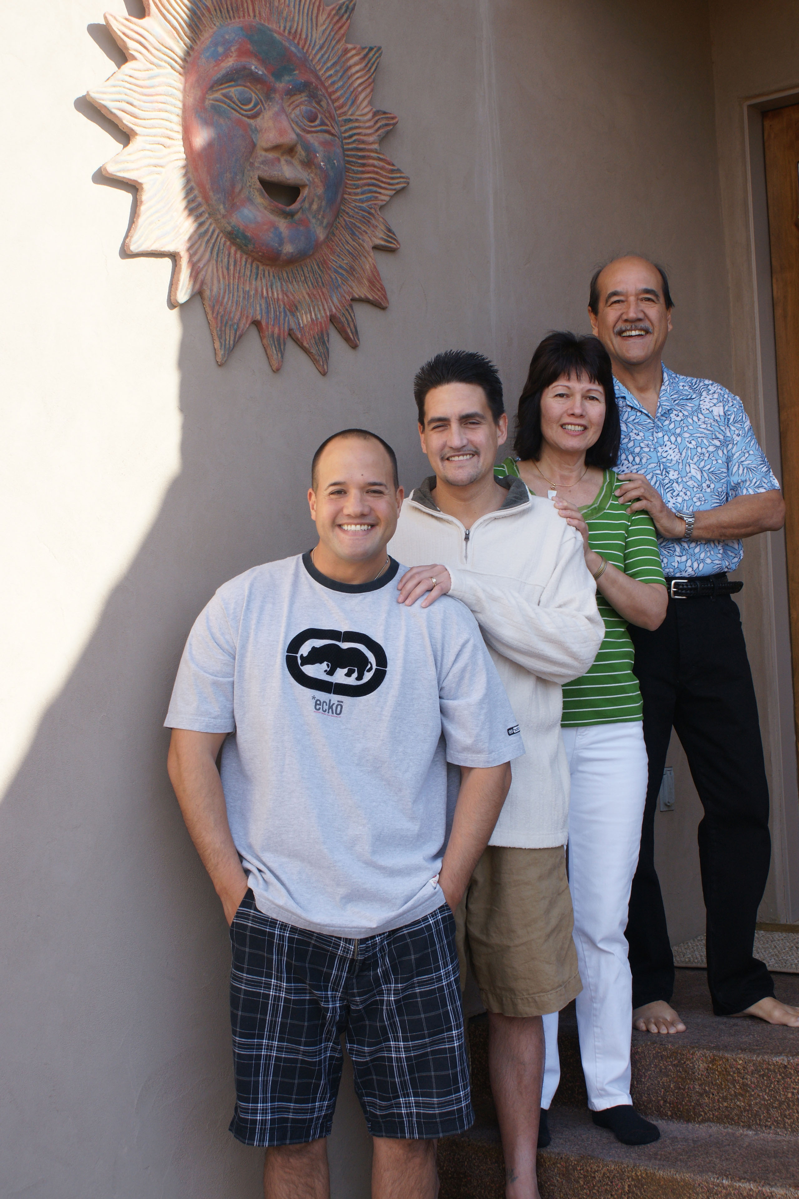 A family portrait taken on the steps of a beige building decorated with a large clay sun. Sheldon Haleck stands in front, on the lowest step, with his brother, Anthony behind him; next is his mother, Verdell; and father, William, on the tallest step.