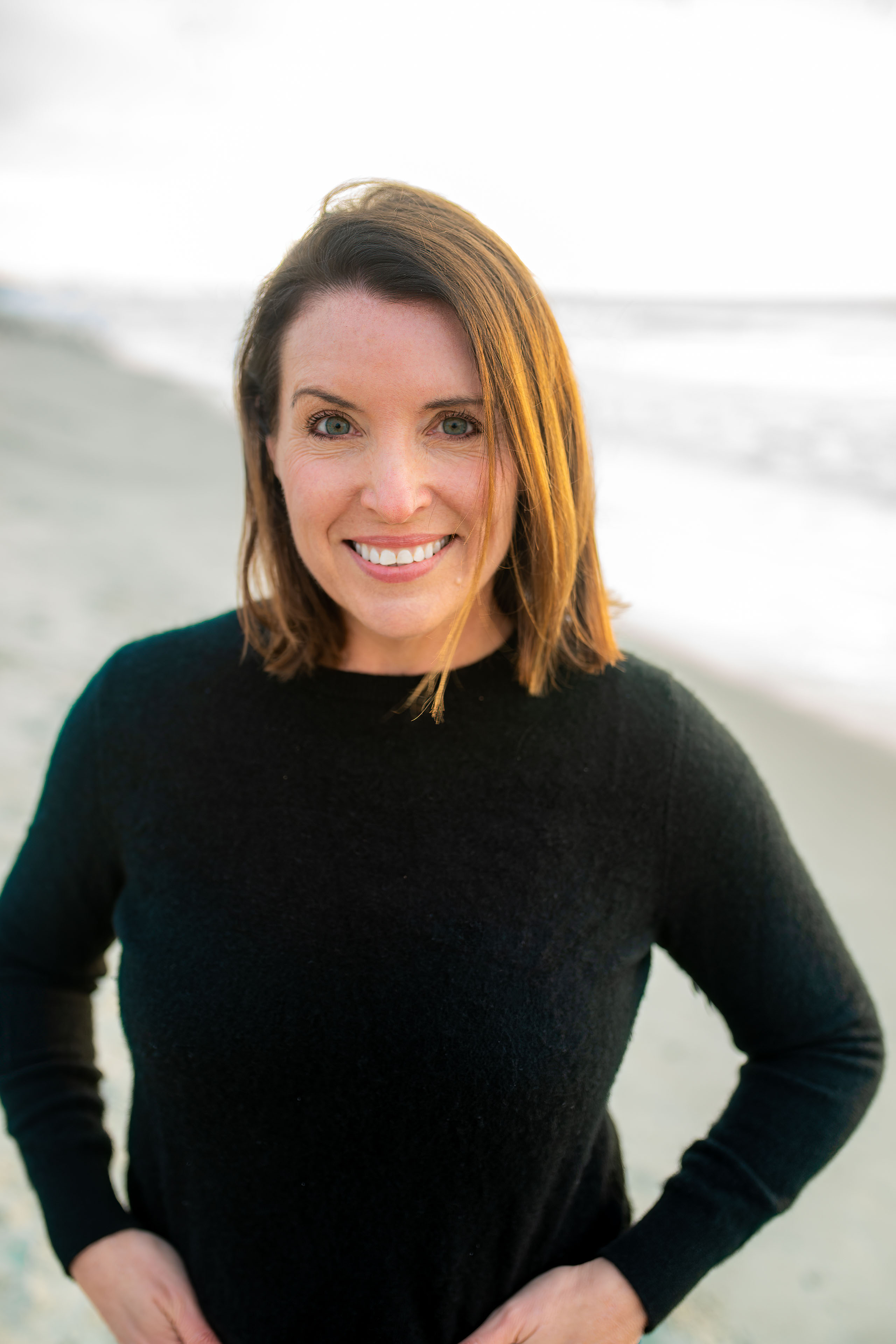 A portrait of Karla Adkins. She is standing outside on a beach and smiles at the camera.