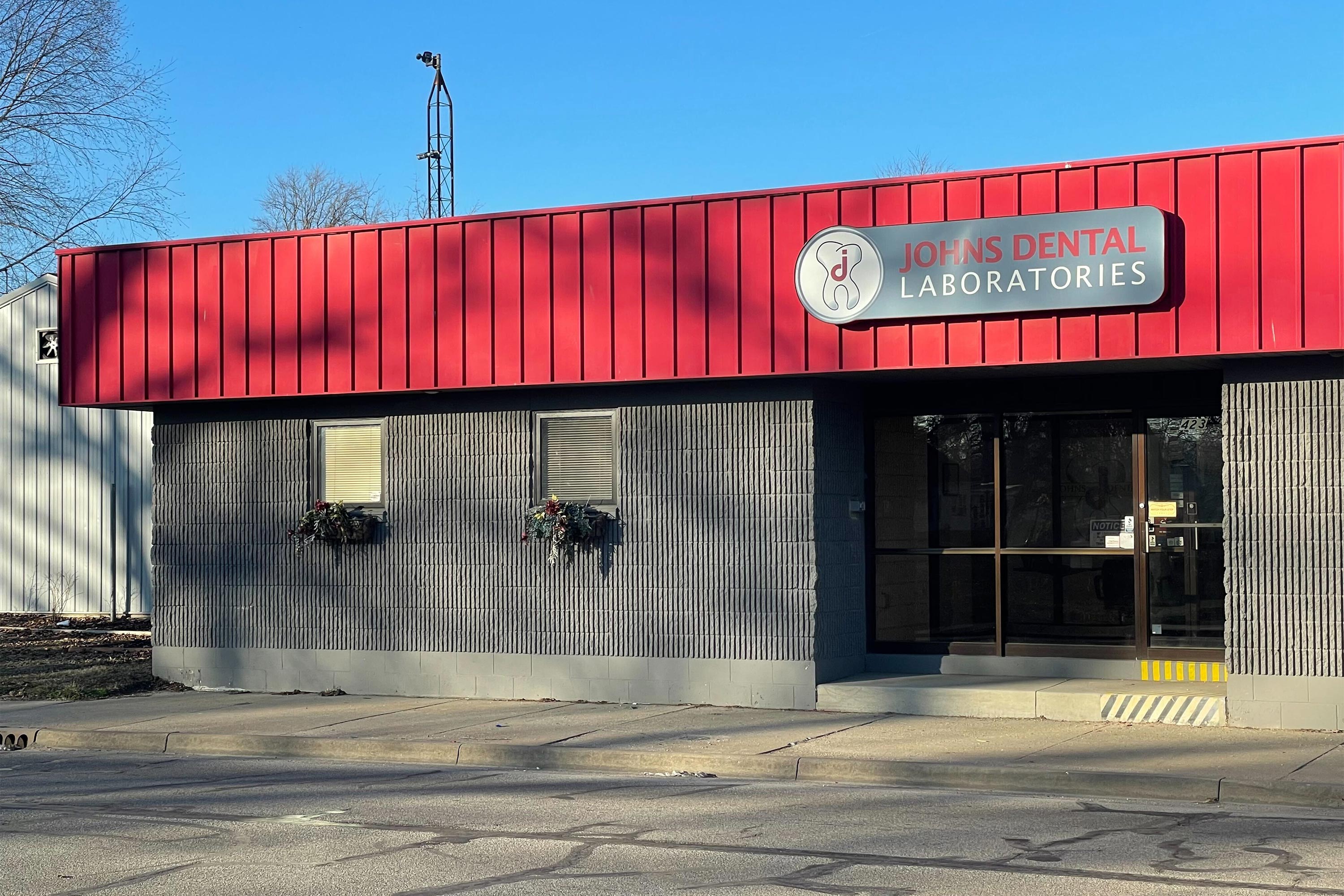 A photo of a building with a red roof, and a sign that reads "Johns Dental Laboratories."