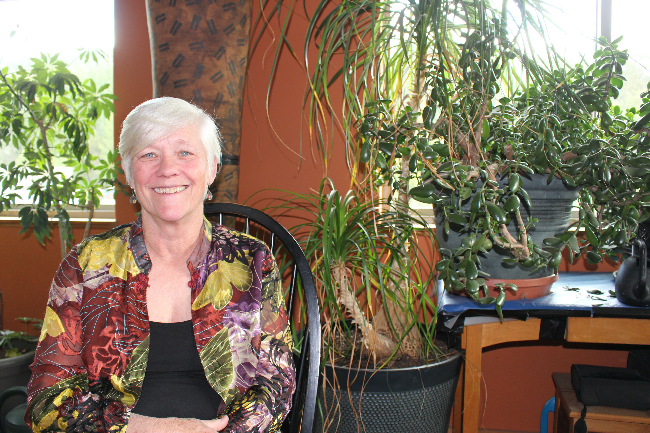 A portrait of Kathryn Larson, who sits in an office overflowing with plants.