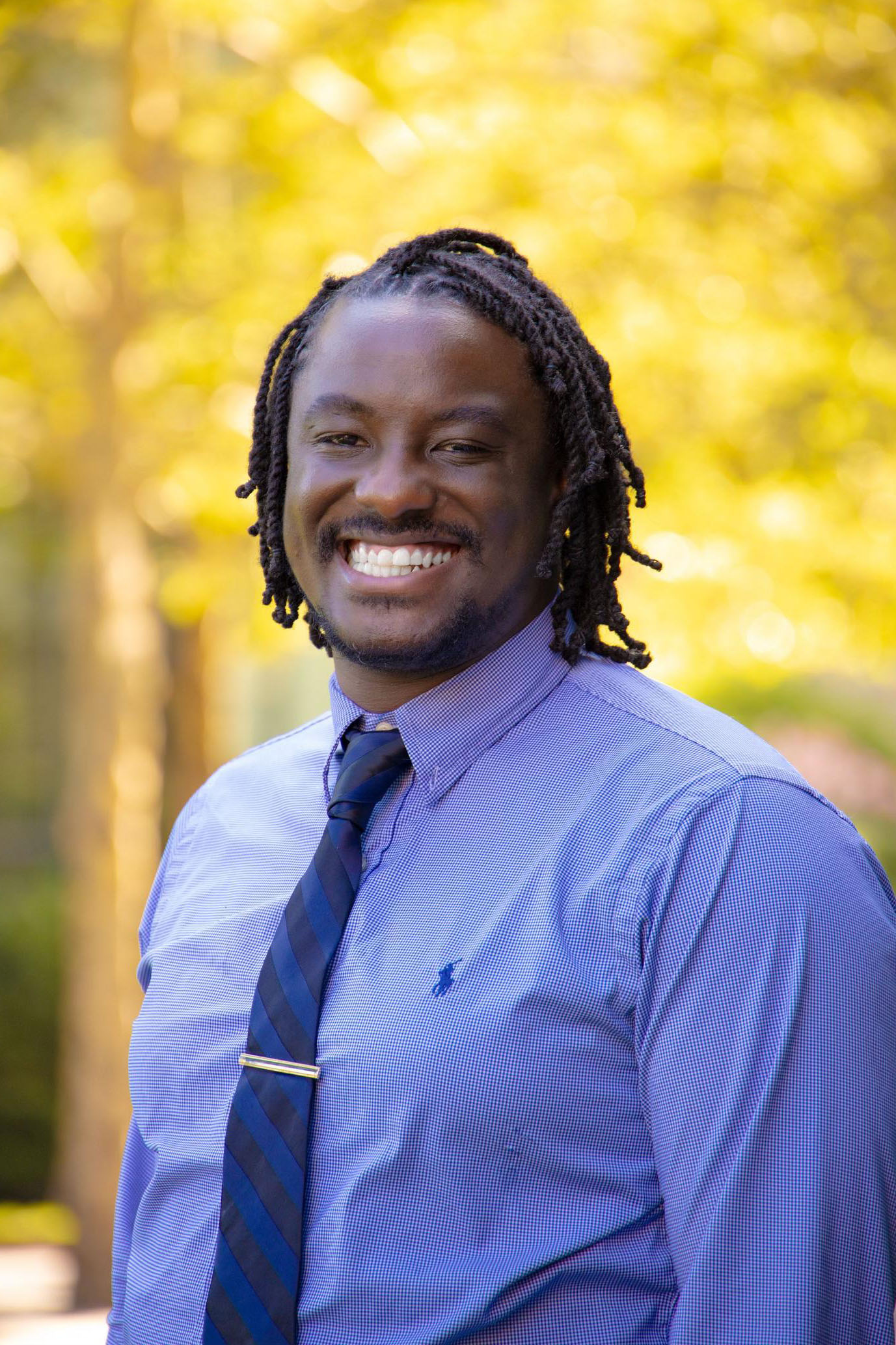A professional portrait of Shannon Brown. He is a young man wearing a blue button down shirt with a blue tie. He smiles broadly toward the camera.