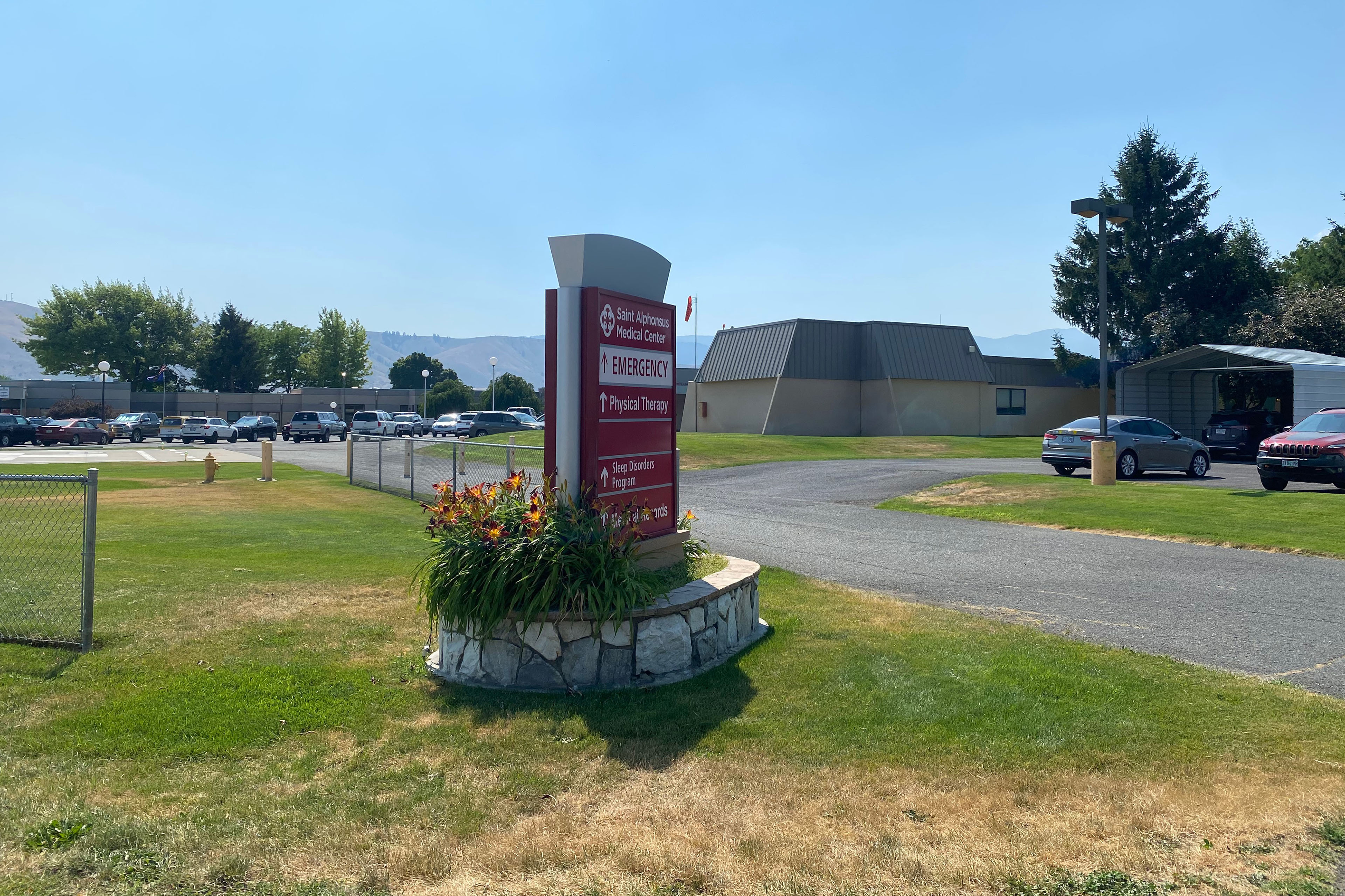 A photograph of the exterior of a medical building on a sunny day. A red sign out front says, "emergency."