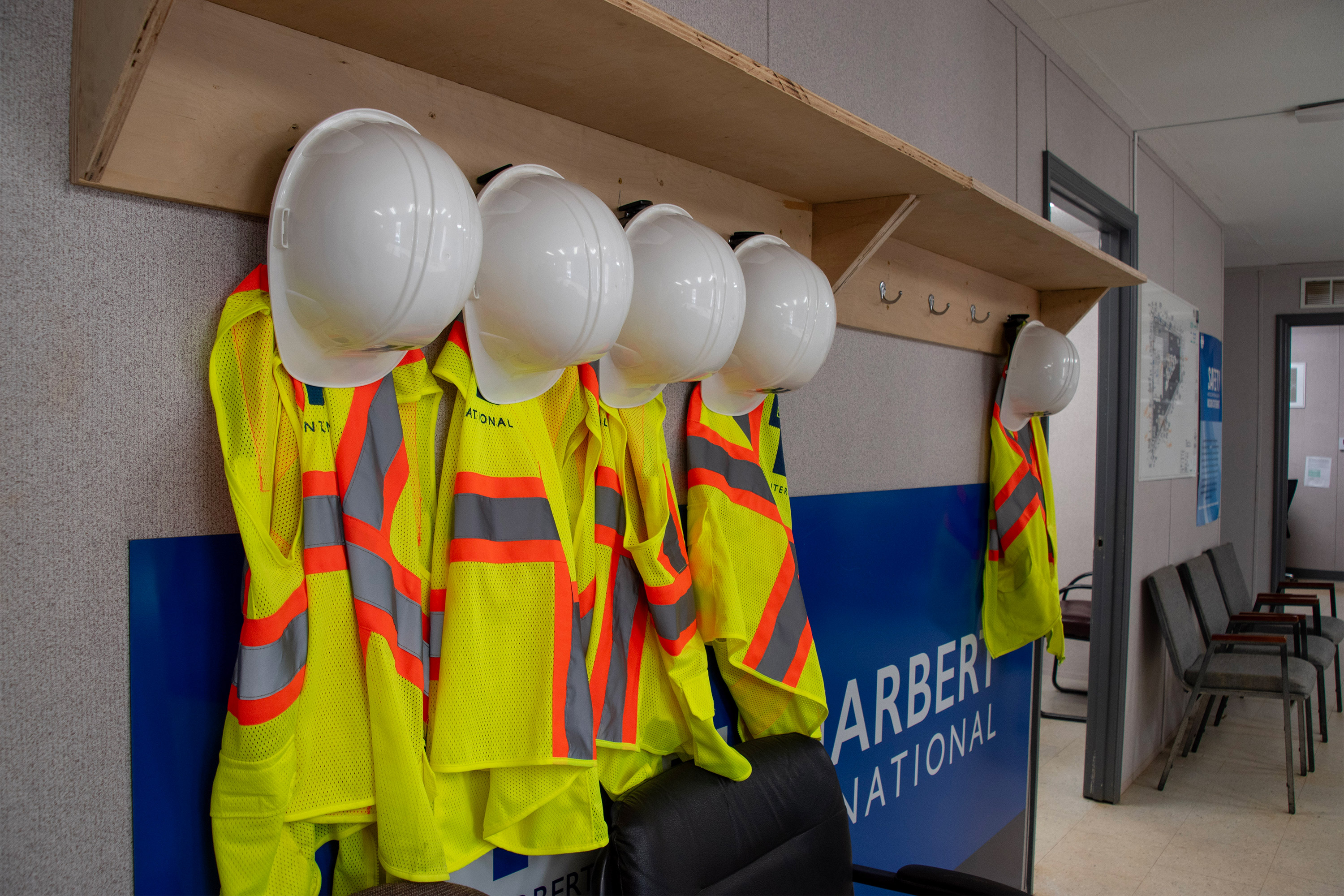 A photo of hard hats and reflective vests hanging on hooks indoors.