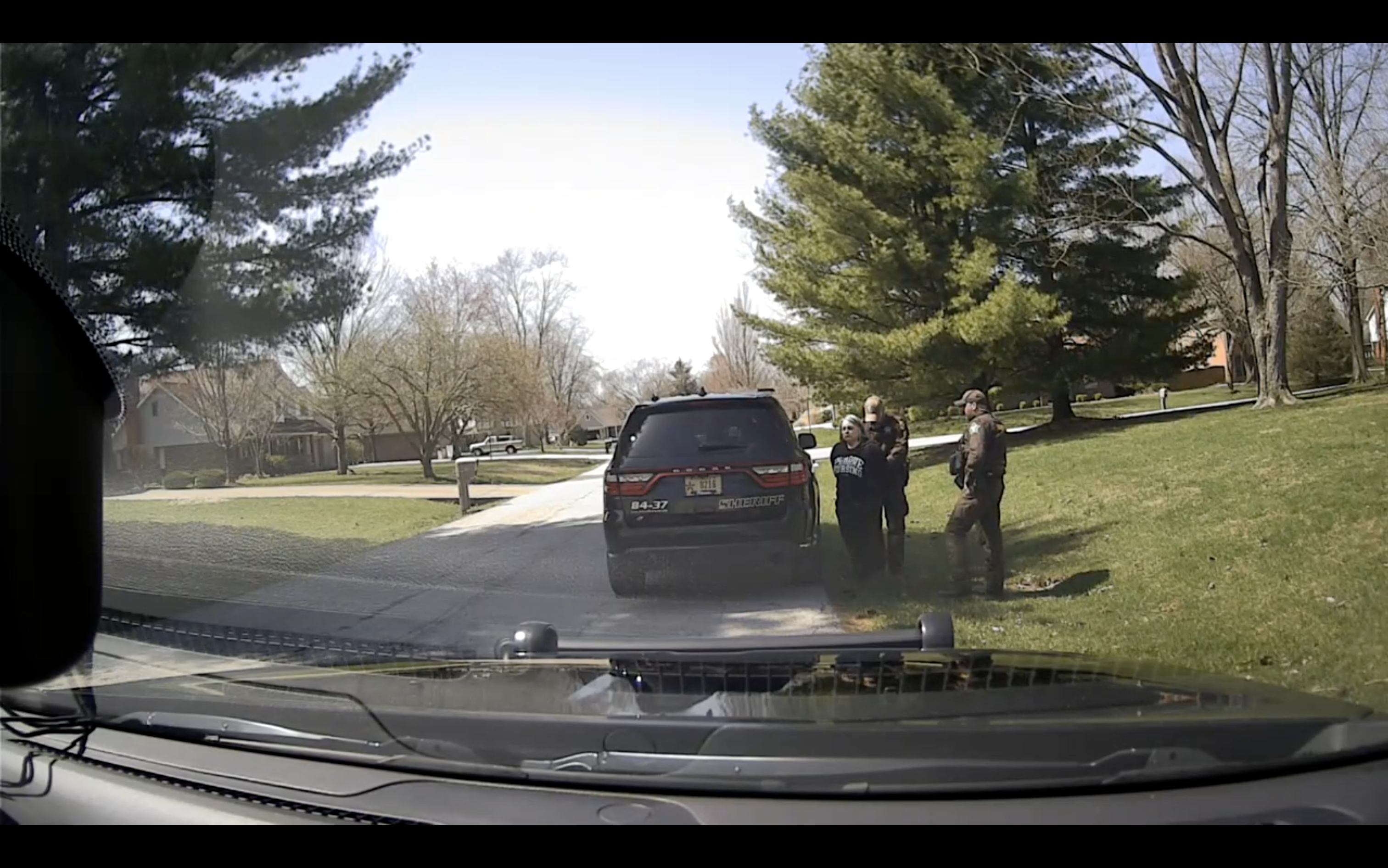 A photo taken from a dashboard camera in a police car shows a woman being handcuffed by a police officer as she stands beside an SUV and a second officer.