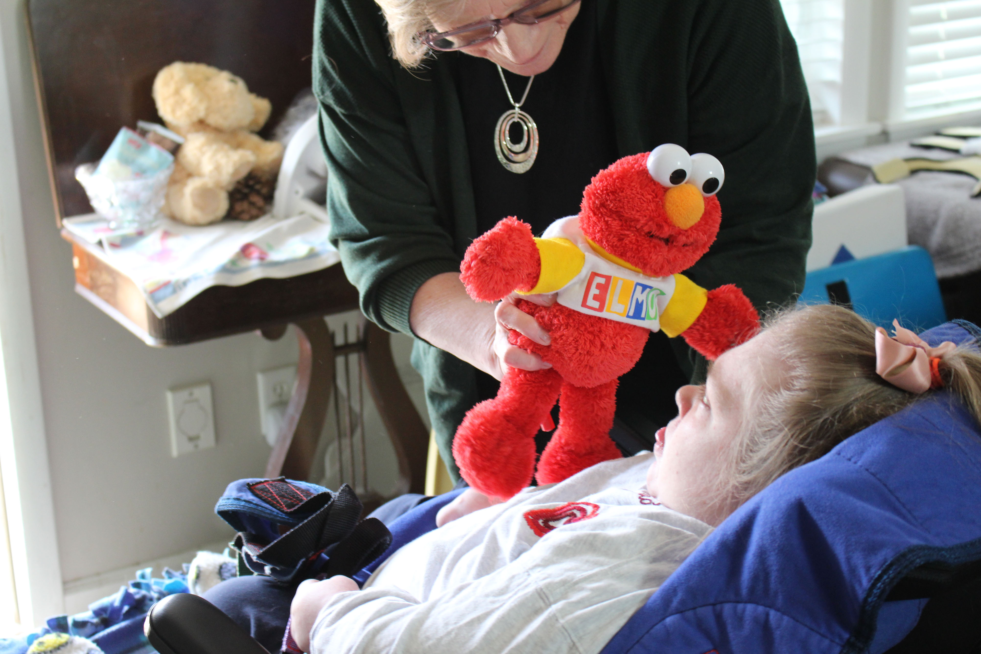 A mother holds an Elmo plush toy in front of her daughter's face.