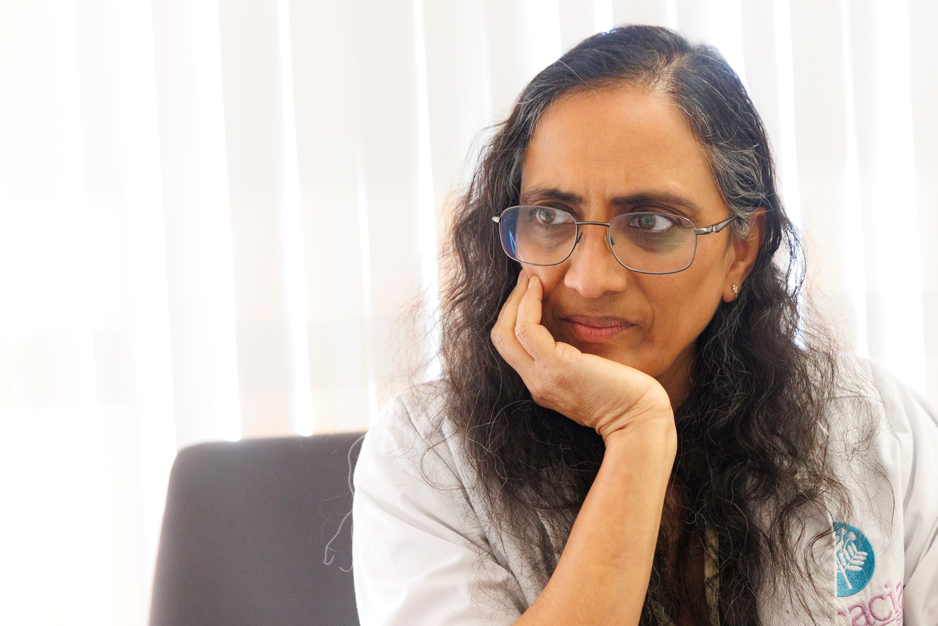 A photo of Sumana Reddy sitting in her office in front of window, looking to the left with a thoughtful expression.