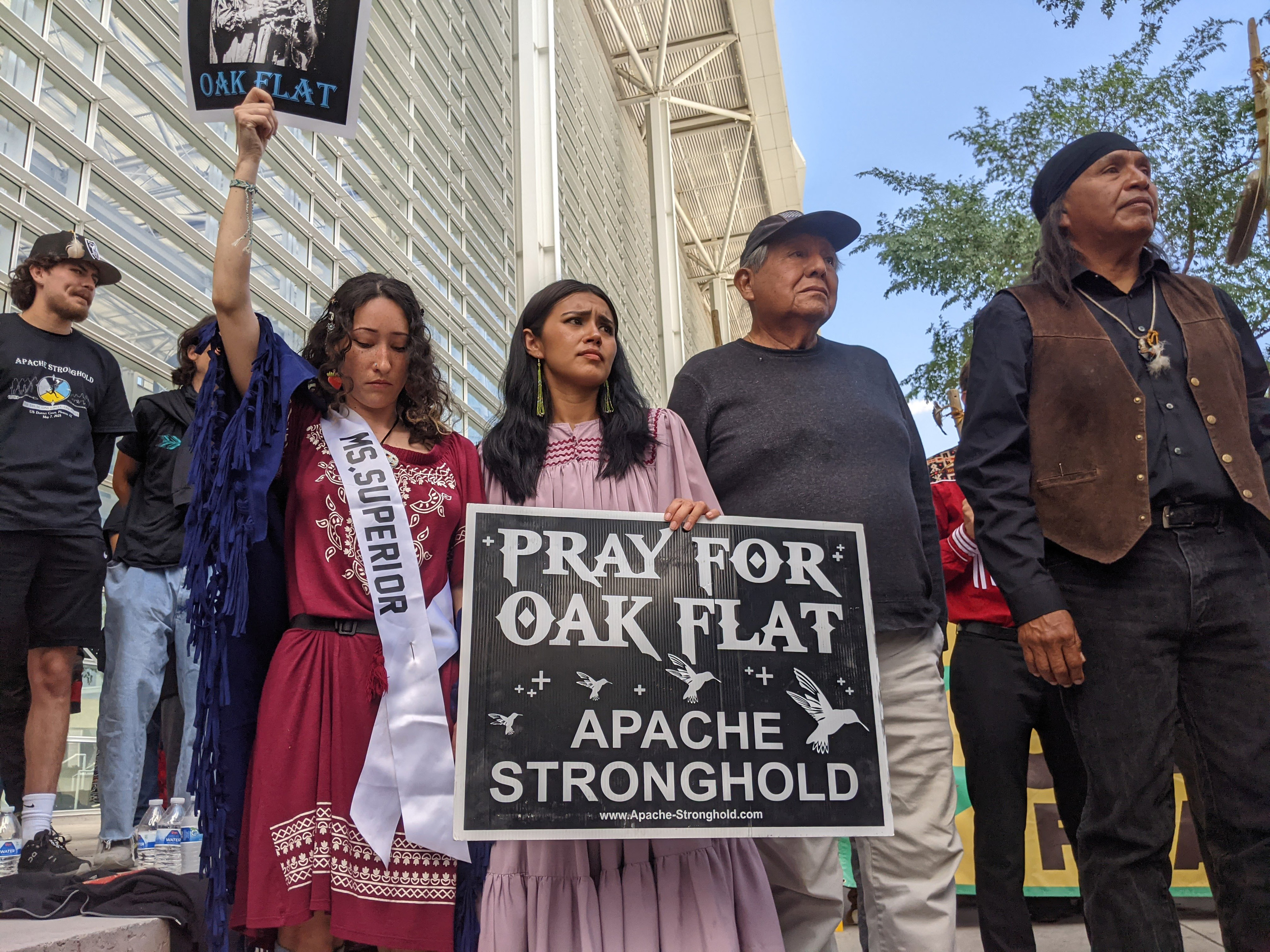 A photo of Nizhoni Pike with her grandfather. Pike holds a sign that reads, "Pray for Oak Flat. Apache Stronghold."