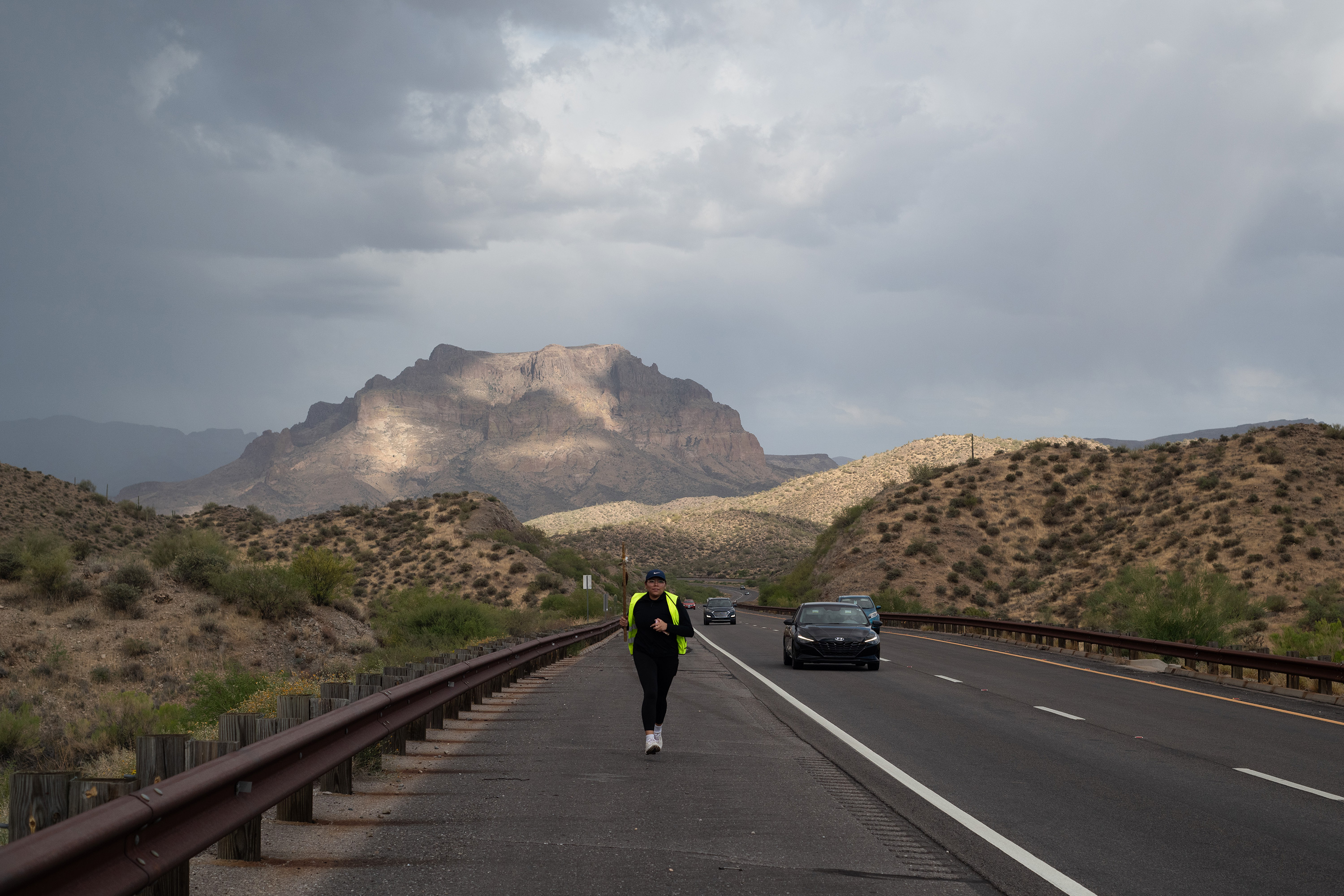 A photo of an indigenous woman running on the side of a highway.