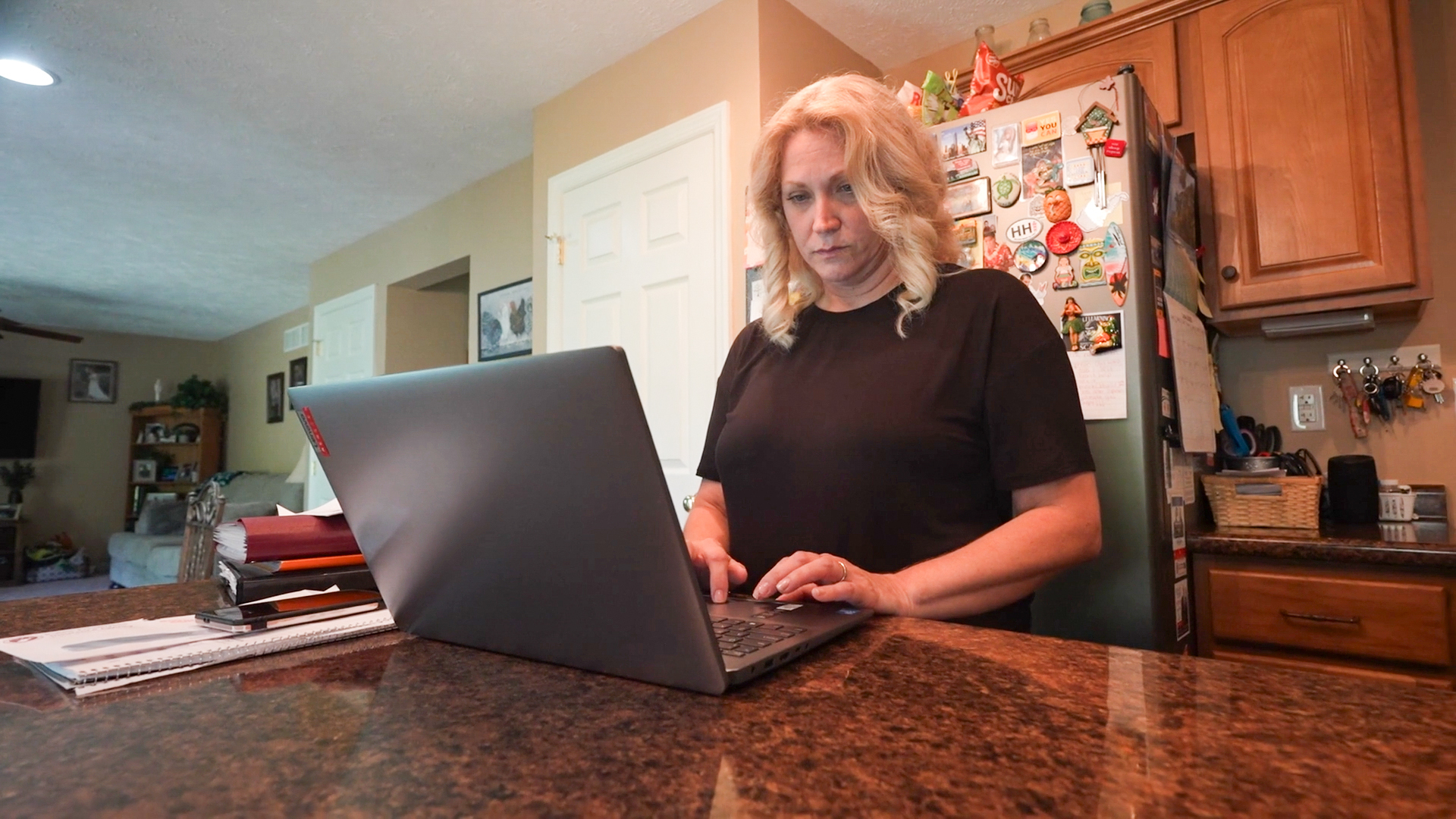 A photo of a woman in her kitchen working on a laptop.