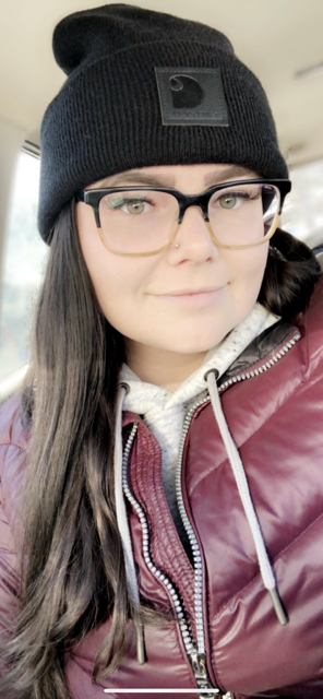 A selfie-style photo of a young woman with long brown hair and glasses.