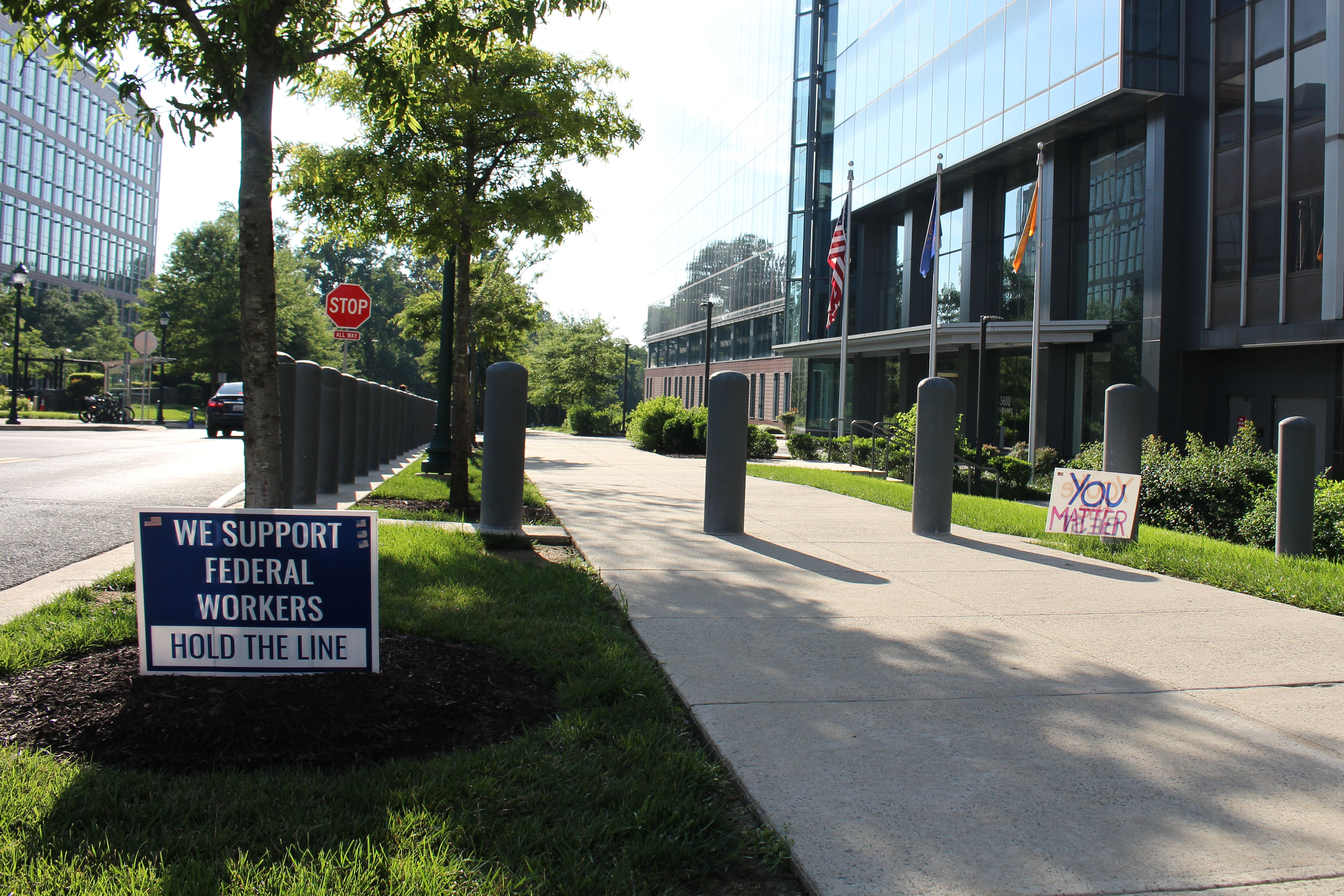 Two lawn signs are beside a sidewalk. They read, "we support federal workers / hold the line," and "you matter."