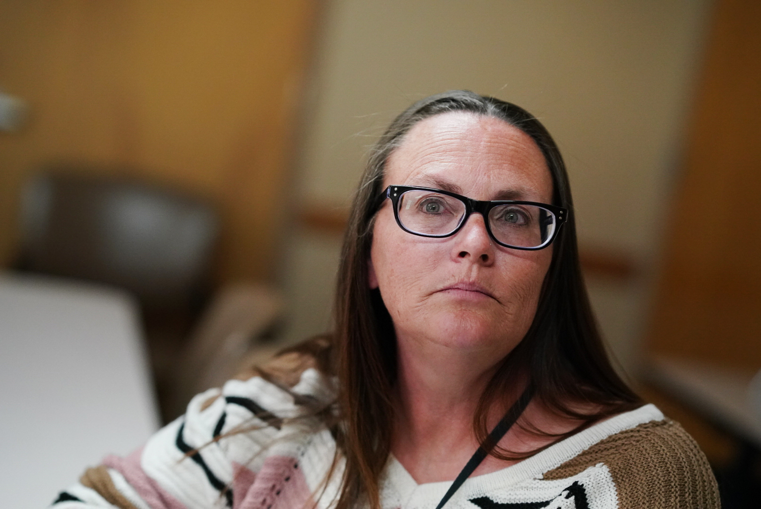 A close photograph of a woman wearing rectangular glasses. She has straight brown hair and wears a patterned sweater.