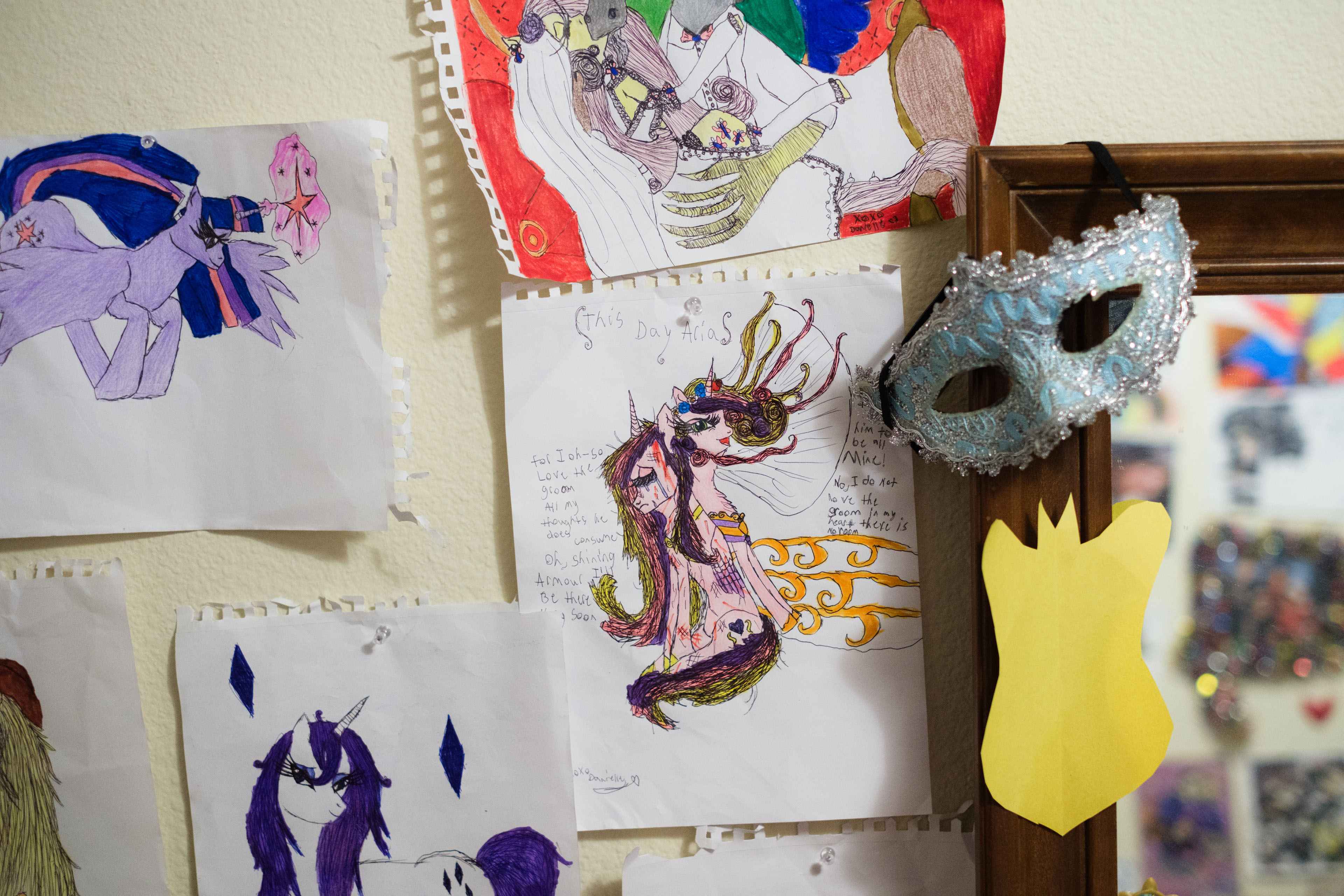 A child's My Little Pony-inspired art is taped up on a wall. The artwork in the center shows a sad and a happy pony facing away from each other.