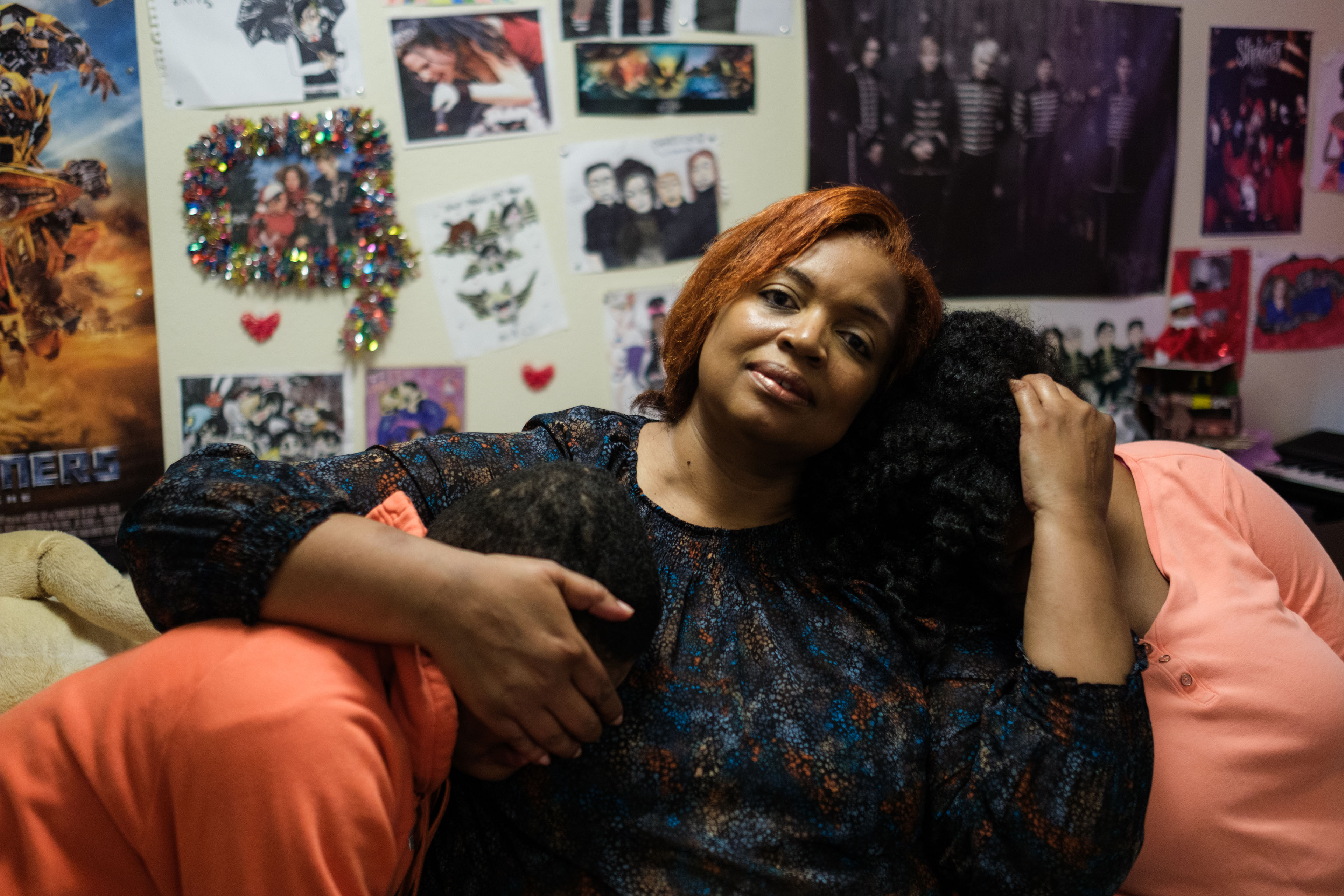 A mother puts her arms around her two children protectively. The children's faces are not visible; the mother looks directly into the camera.