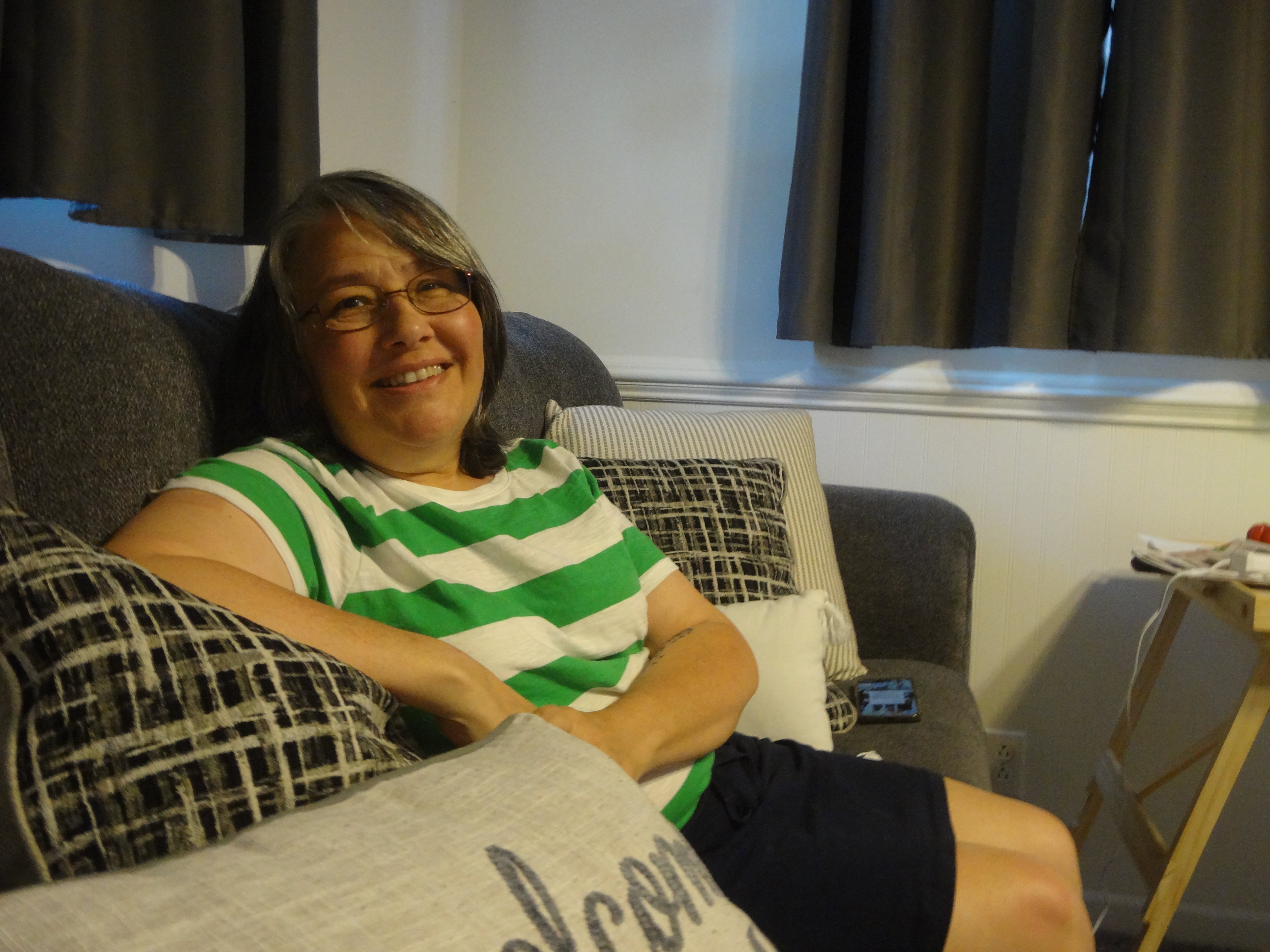 A woman with glasses and a green and white striped tshirt sits on a couch 