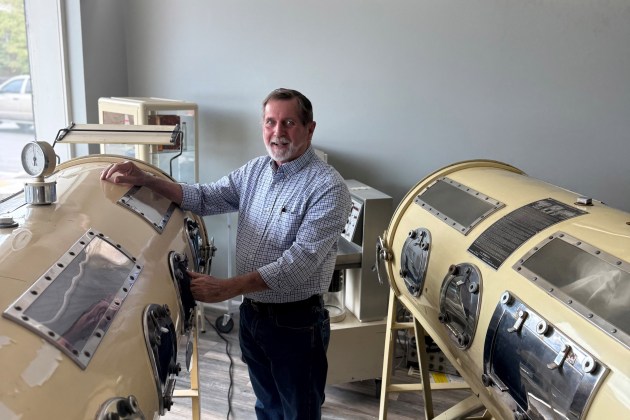 A man stands with his hands on a large, yellow metal tube