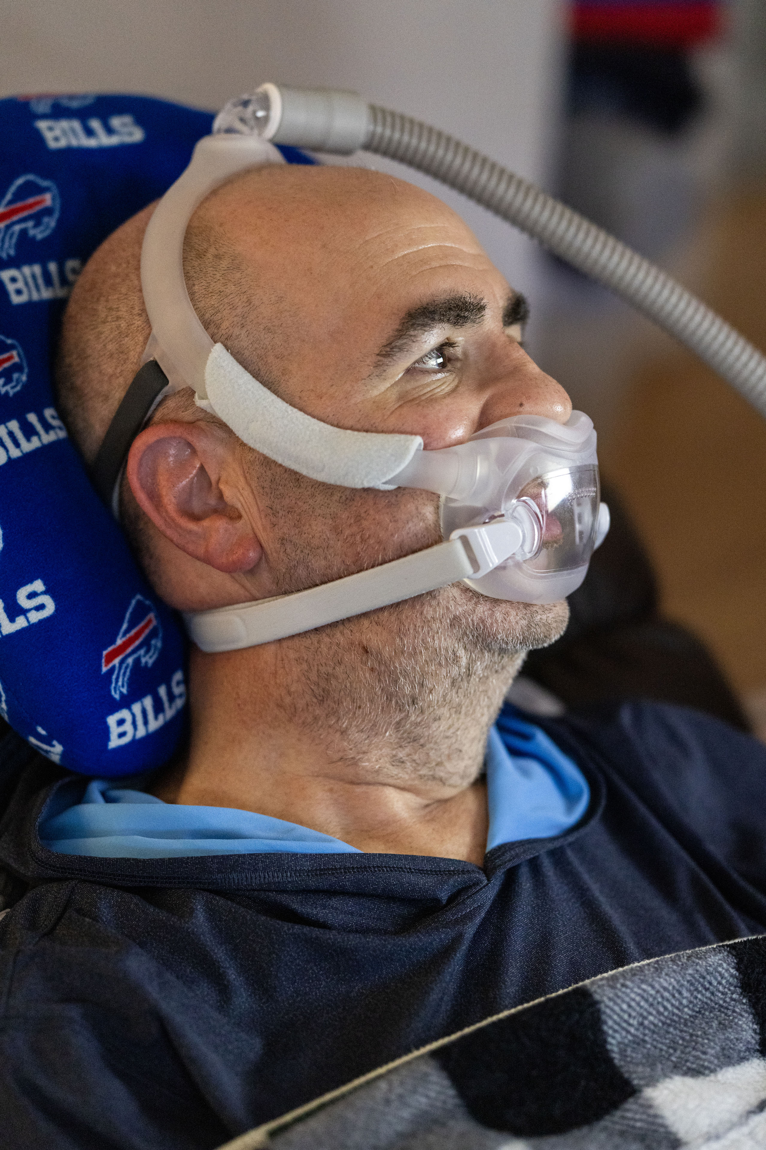 A man leans back on a Buffalo Bills pillow while wearing a breathing mask