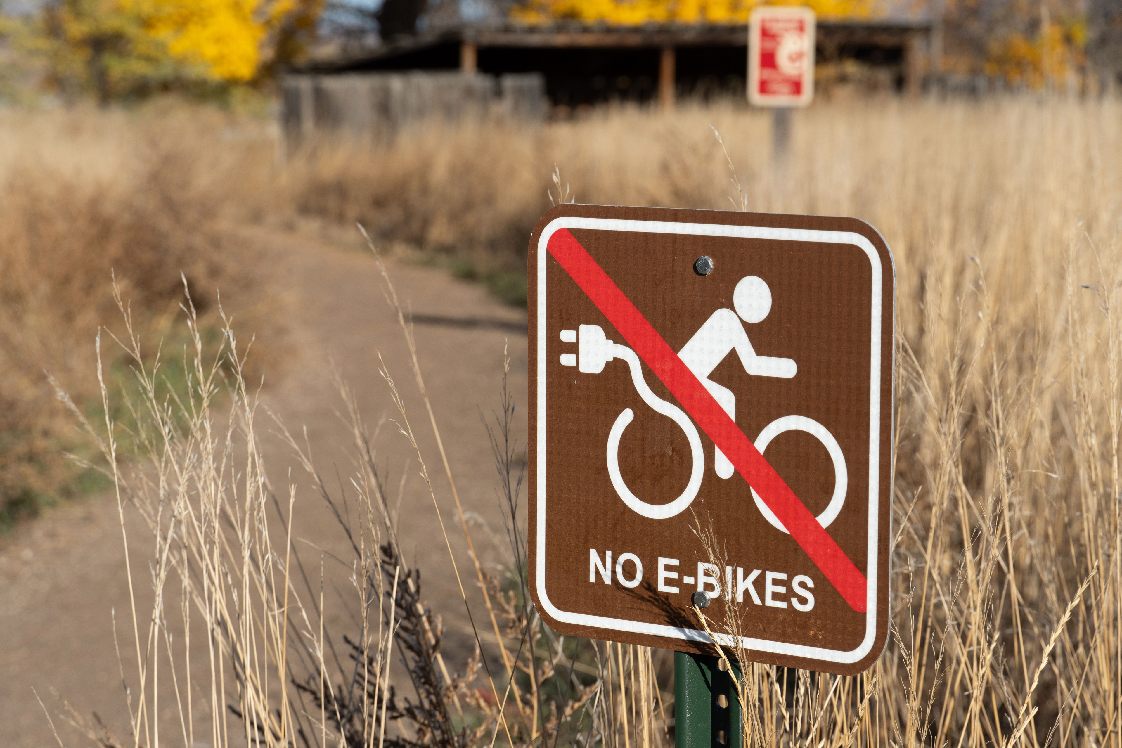 A small brown sign of an e-bike cyclist crossed out with a red line. Text reads, "No e-bikes."