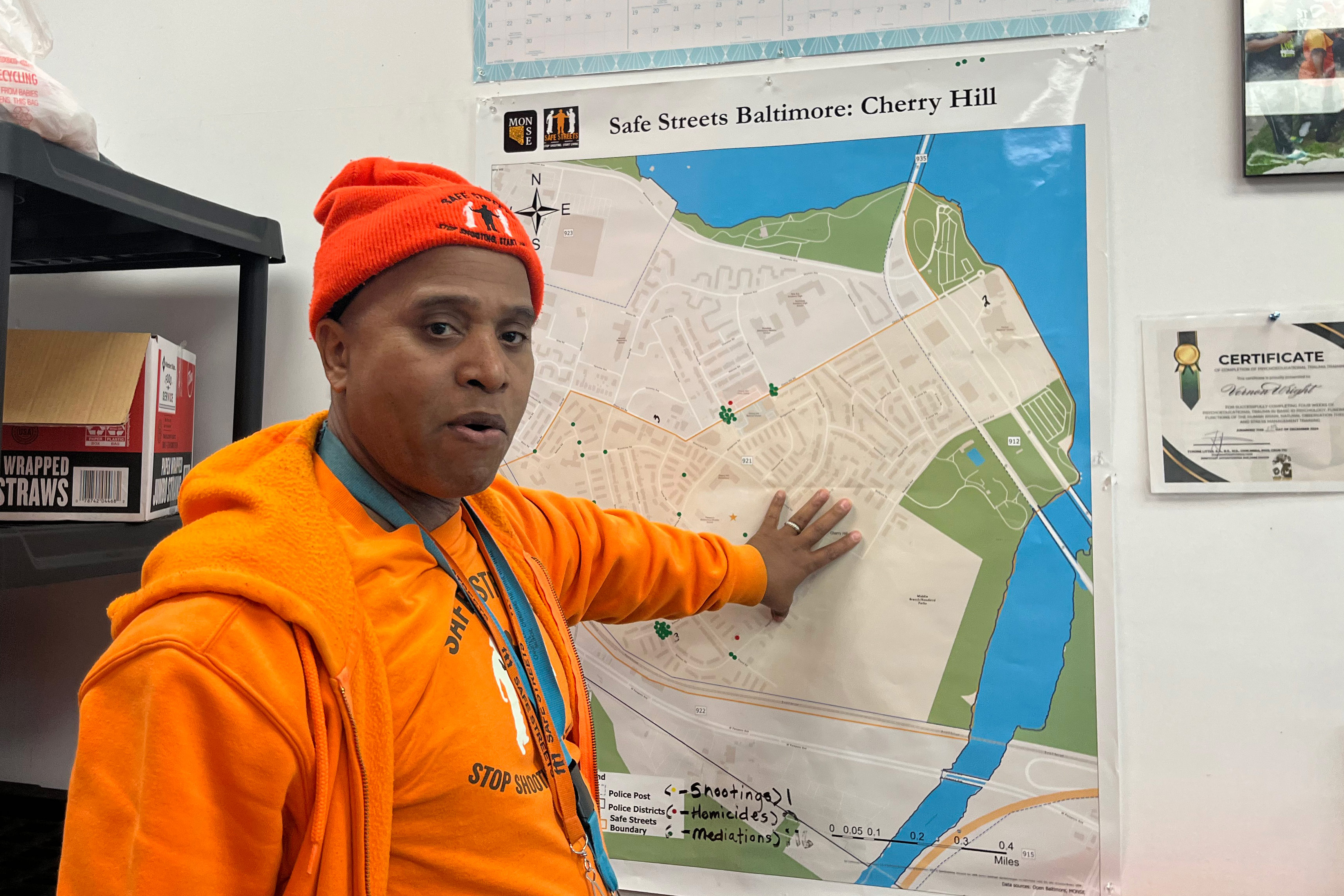 A photo of a Safe Streets worker in bright orange. He points to a map of Baltimore's Cherry Hill neighborhood.