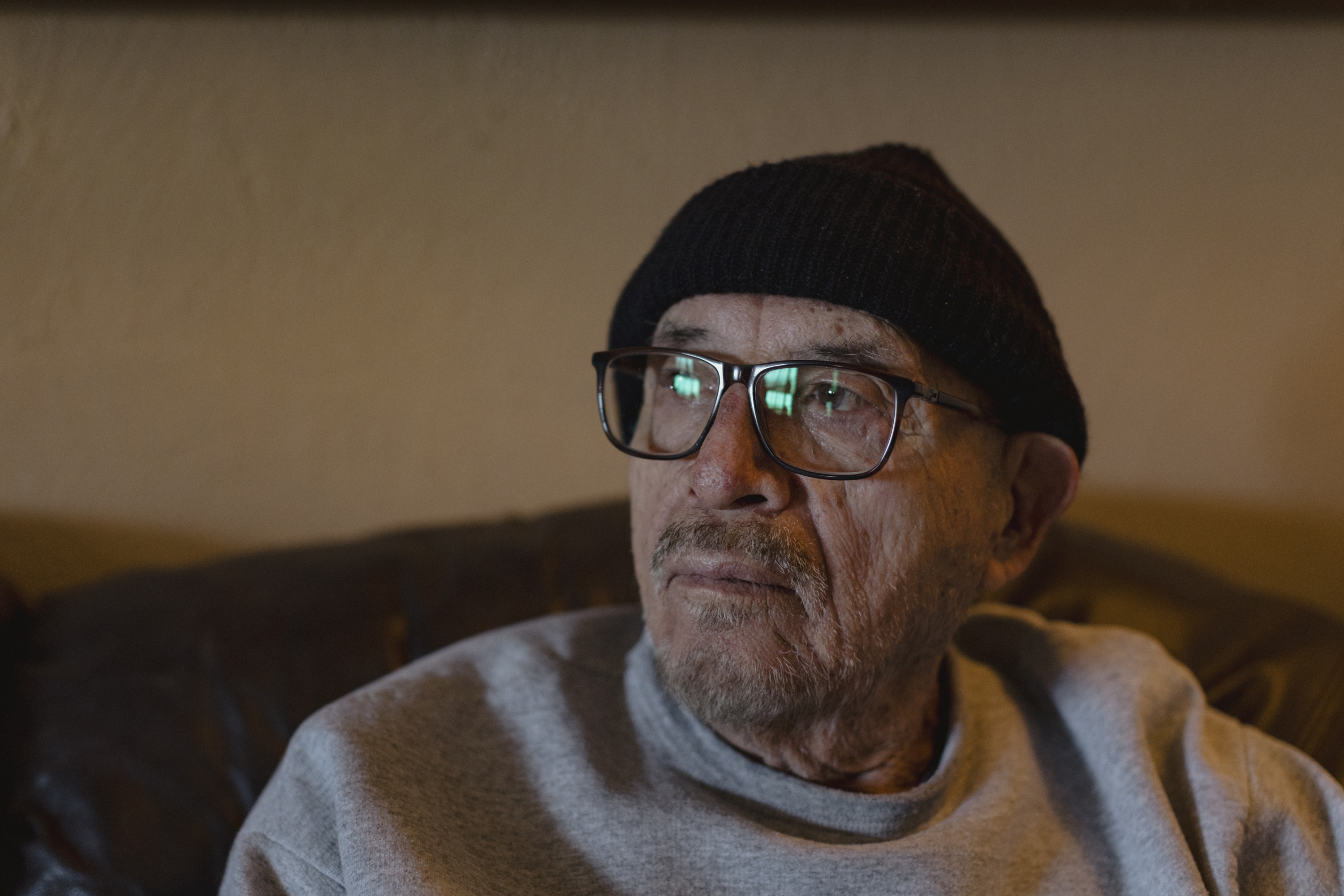 A man wearing black-rimmed glasses and a black hat looks away from the camera
