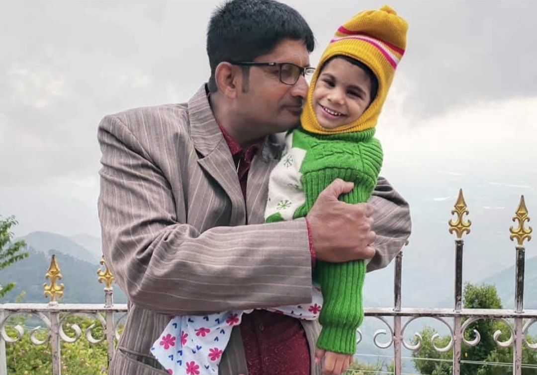 A fatheri holds his young daughter, who is wearing a knit cap.