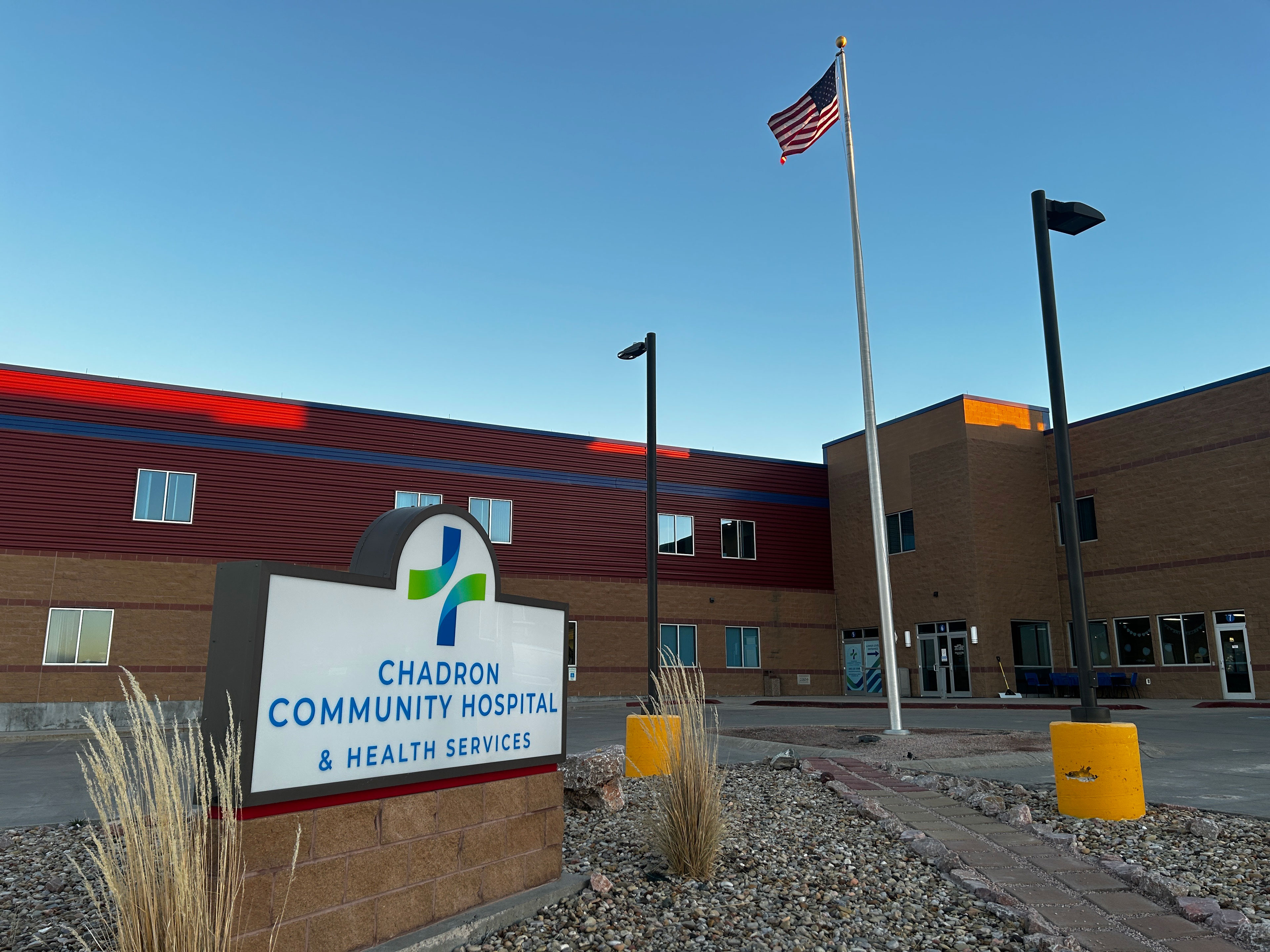 An exterior shot of a hospital in Nebraska. A sign out front reads, "Chadron Community Hospital & Health Services." An American flag flies on a flagpole behind it.